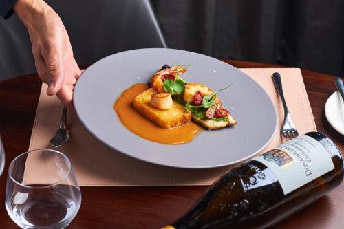 a person holding a plate of food and a bottle of wine at InterContinental Malta by IHG in St Julian's
