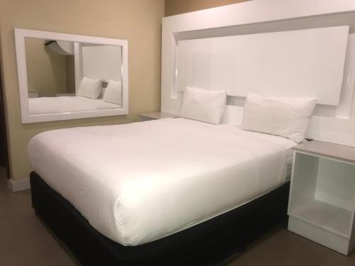 PALACE LODGE PINETOWN في بينتاون: سرير أبيض كبير في غرفة مع مرآة