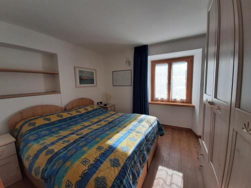 Un dormitorio con una cama con un edredón colorido y una ventana en NUOVISSIMO BILOCALE PALAZZINA VENERI en Cogolo