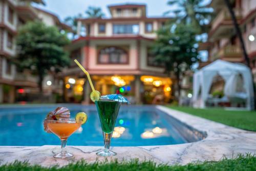 two cocktails sitting on a table next to a swimming pool at Lillywoods Highland Beach Resort- Candolim in Candolim