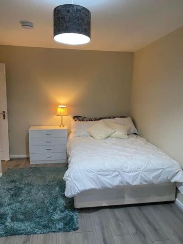 a bedroom with a white bed with a night stand and a lamp at Dorcas Lodge - Lovely 5 Bedroom home with free parking and Wi-Fi in Nevendon