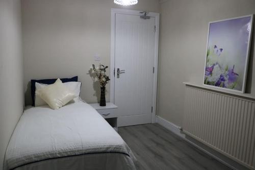 a white bedroom with a bed and a vase of flowers at Dorcas Lodge - Lovely 5 Bedroom home with free parking and Wi-Fi in Nevendon