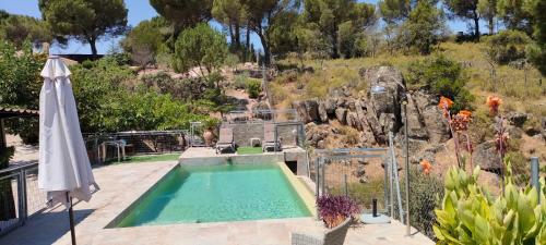 a swimming pool with an umbrella next to a garden at CABAÑA DE MADERA JUNTO AL LAGO LAS JARAS in Córdoba