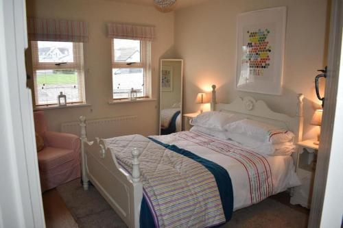 a bedroom with a white bed and two windows at Holiday Home- Portballintrae in Portballintrae