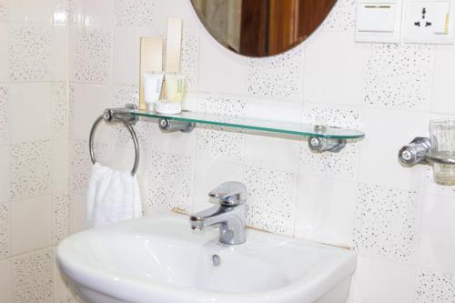 lavabo blanco en el baño con espejo en Lou Ralph Hotel, en Accra