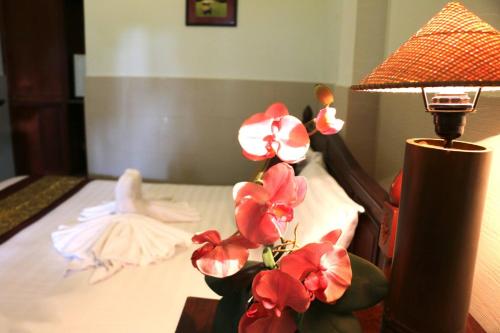 a table with a lamp and flowers on a bed at Mali Namphu Hotel in Vientiane