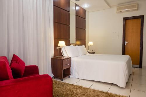 um quarto de hotel com uma cama e uma cadeira vermelha em Ibituruna Center Hotel em Governador Valadares