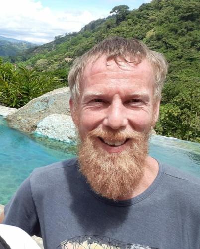 a man with a beard standing next to a body of water at Montaña Linda Hostel Orosi in Orosí