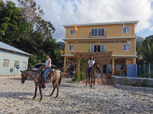 two people riding horses in front of a building at Hotel y Restaurante Virgen de Fátima in La Ceiba