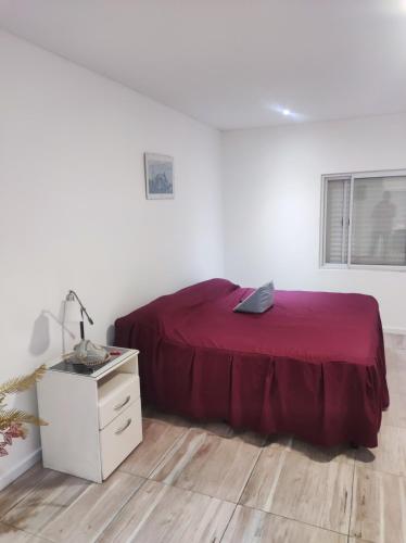 a white bedroom with a red bed and a desk at DEPARTAMENTO MONO AMBIENTE in Reconquista