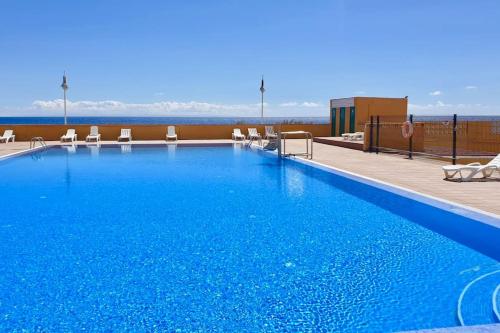 ein großer blauer Pool mit Stühlen und das Meer in der Unterkunft Ocean View Apartment Poris in Poris de Abona