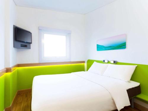 a green and white bedroom with a bed and a television at Ibis Budget Bandung Asia Afrika in Bandung