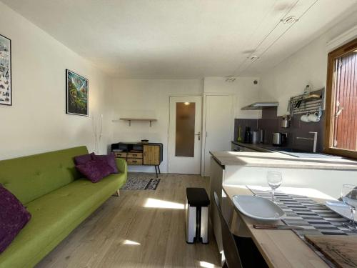un salon avec un canapé vert et une cuisine dans l'établissement Appartement cosy à Serre-Chevalier, proche pistes, terrasse, parking, 2 étoiles, 2 pers. - FR-1-330E-127, à Saint-Chaffrey