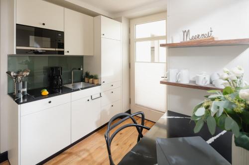 a kitchen with white cabinets and a table and chair at J Huus 4 I 99m I Strand I Kurplatz I EG I Terrasse I Ruhig I King I FB Heizung I Privateingang I Huus Design in Norderney