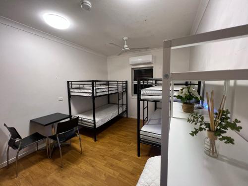 a room with three bunk beds and a table and a desk at Tomato Backpackers in Bundaberg