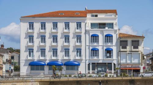 un bâtiment blanc avec des auvents bleus sur le côté d'une rivière dans l'établissement CERISE Royan - Le Grand Hôtel de la Plage, à Royan