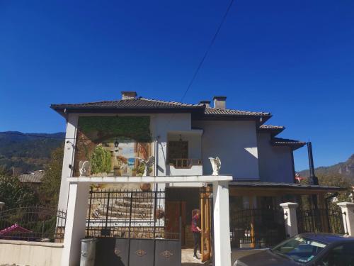 a blue house with a woman standing outside of it at Къща Томови,стаи за гости in Devin