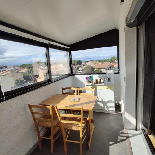 une table et des chaises dans une pièce avec des fenêtres dans l'établissement Appartement cosy proche port, plages et montagnes., à Saint-Cyprien