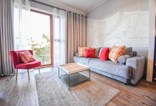 a living room with a couch and a red chair at Apartamenty Na Wyspie - Baltic Park - Apartamenty z sypialnią i parkingiem - ul Uzdrowiskowa 24-34 in Świnoujście