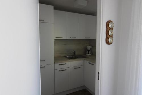 eine Küche mit weißen Schränken, einer Spüle und einer Uhr in der Unterkunft Haus Nordseeresidenz Wohnung 63 in Westerland