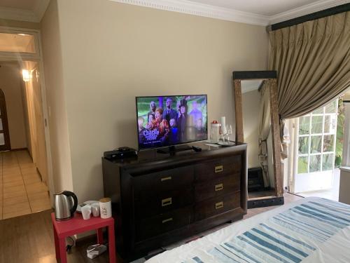 a bedroom with a bed and a television on a dresser at Safari Apartments -Beautiful 3 bedrooms, 10-seater dining , TV room, Garden & Pool in Johannesburg