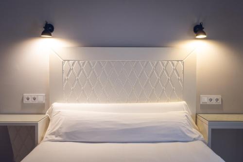a bedroom with a white bed with two lights on it at Hostal Los Castañuelos in Candeleda