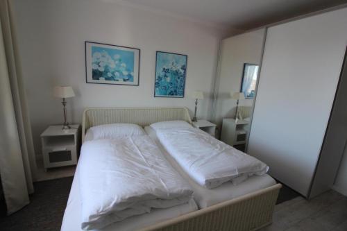 1 dormitorio con 1 cama con sábanas y almohadas blancas en Haus Norderhoog Wohnung 64, en Westerland