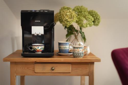 a coffee maker on a table with cups and a plant at Apartamenty U Harrego I Przy Stawie Spa z klimatyzacją, balia, sauna, ogrodem i parkingiem in Kudowa-Zdrój