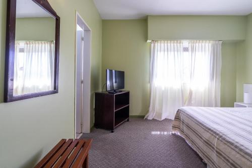 1 dormitorio con 1 cama, TV y espejo en Hotel Arte del Rey en Pinamar