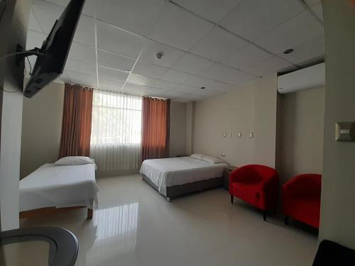 Cette chambre d'hôtel comprend deux lits et un fauteuil rouge. dans l'établissement Hospedaje bolognesi, à Piura