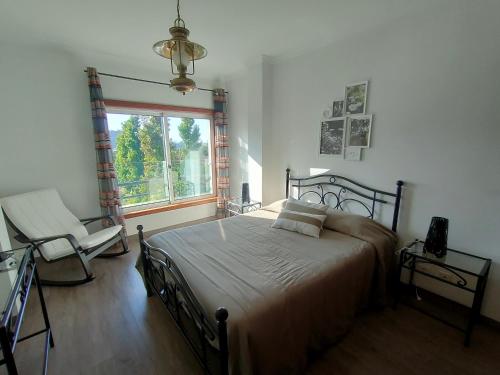 a bedroom with a bed and a chair and a window at Alto Minho Central Apartment in Paredes de Coura