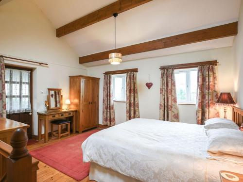 a bedroom with a bed and a desk and windows at Curlew Cottage in Bromlow