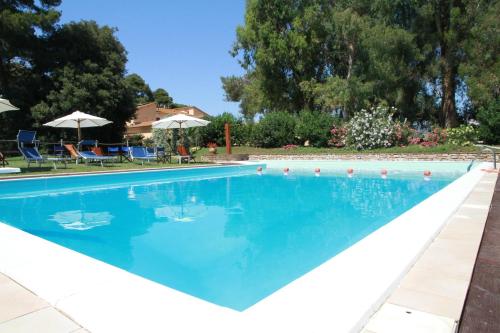 a swimming pool with blue water and chairs and umbrellas at Agriturismo La Ronca in San Vincenzo