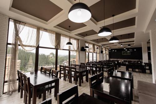 um restaurante com mesas e cadeiras e janelas grandes em Toga cottage em Yablunytsya