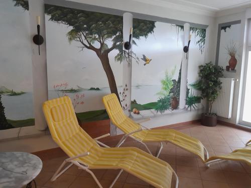 a room with two yellow chairs and a tree on the wall at Ferienanlage - Zum See & Hotel in Plau am See