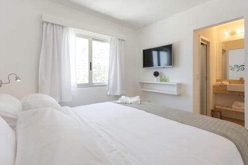 a white bedroom with a bed and a tv at 20 Hotel in Punta del Este