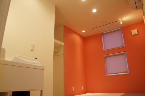 a bathroom with an orange wall and two windows at SORAYADO 宙宿 in Tsuru 