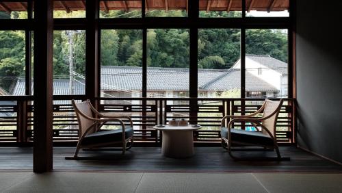 2 sillas y una mesa en una habitación con ventanas en Kobayashiya -Kinosaki Onsen-, en Toyooka