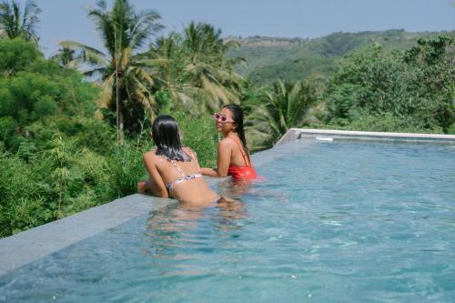 two women sitting on the edge of a swimming pool at PORTER HOTEL - Surf & Yoga Retreat in Kuta Lombok