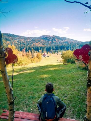 a man with a backpack sitting in a field with a view at Apartmani ZELENI MEDA in Mitrovac