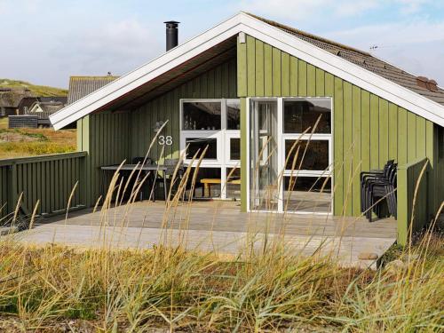 a green building with a wooden deck in front of it at 4 person holiday home in Hvide Sande in Bjerregård