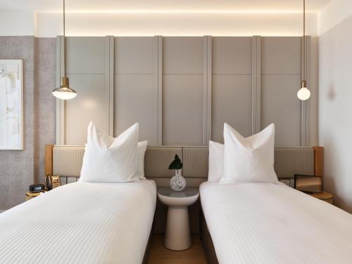 two beds in a hotel room with white pillows at The Porter House Hotel Sydney - MGallery in Sydney