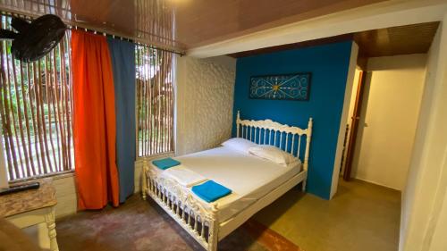 Cama pequeña en habitación con paredes y ventanas azules en WAYANAY TAYRONA ECO HOSTEL, en El Zaino