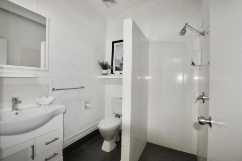 a white bathroom with a toilet and a sink at Hideaway Noosa Men Only Beach Resort in Peregian Beach