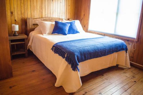 a bedroom with a bed with blue sheets and a window at Casa Pehuen, Cabañas in Villarrica