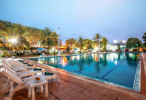 a large swimming pool with chairs and palm trees at Surabaya Suites Hotel Powered by Archipelago in Surabaya