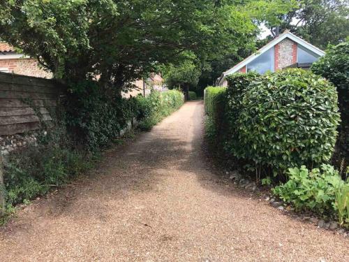 a dirt road next to a house with a hedge at Lovely quiet cottage Sleeps 4 adults, 4 children, Dog Friendly in Cley next the Sea
