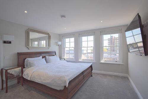 Schlafzimmer mit einem großen Bett mit weißer Bettwäsche und Fenstern in der Unterkunft Harper Luxe Serviced Apartments Dunstable in Dunstable