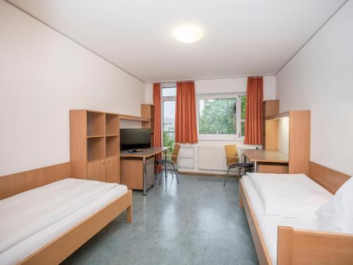 a hotel room with two beds and a desk and a kitchen at Kolpinghaus Salzburg in Salzburg