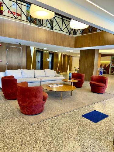 a living room with a white couch and red chairs at Comfort Hotel Fortaleza in Fortaleza